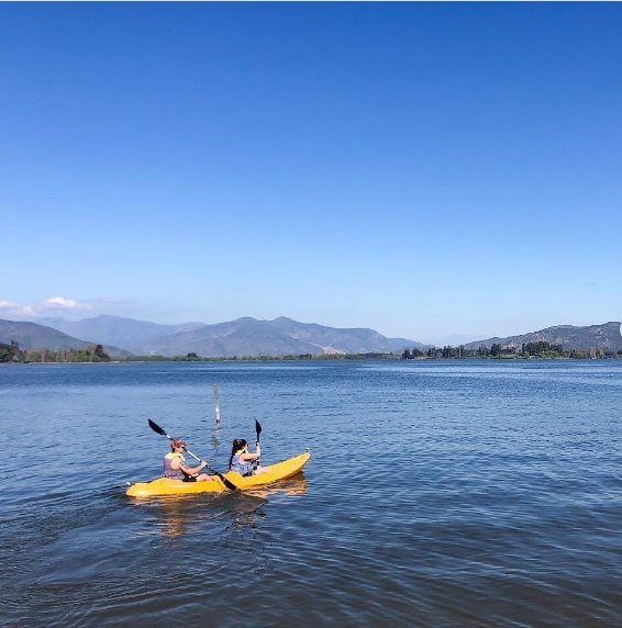 Dos personas remando en un kayak amarillo en el Lago Rapel, con los cerros al fondo